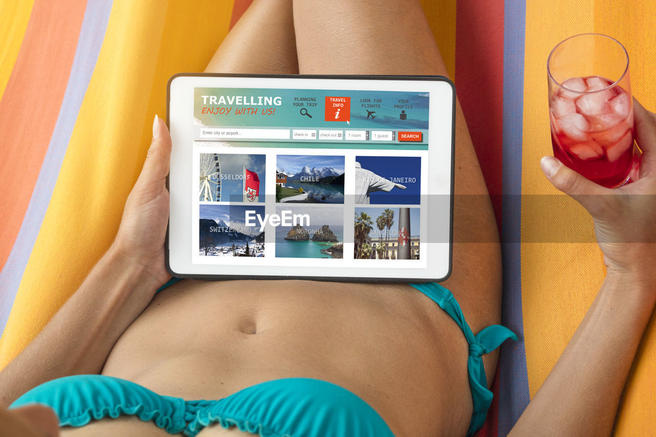 Midsection of woman having drink while using digital tablet in hammock