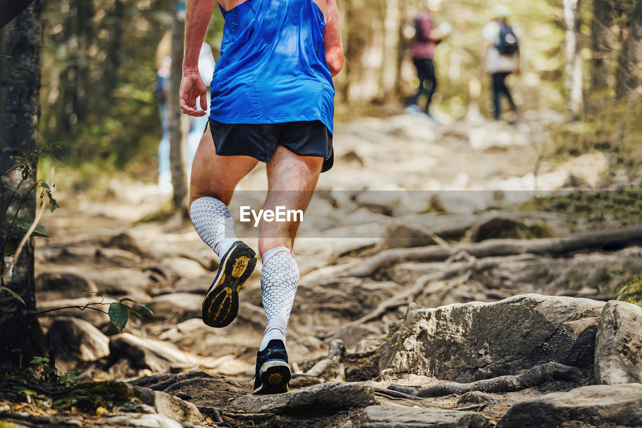Male runner in compression calf sleeve run over rocks