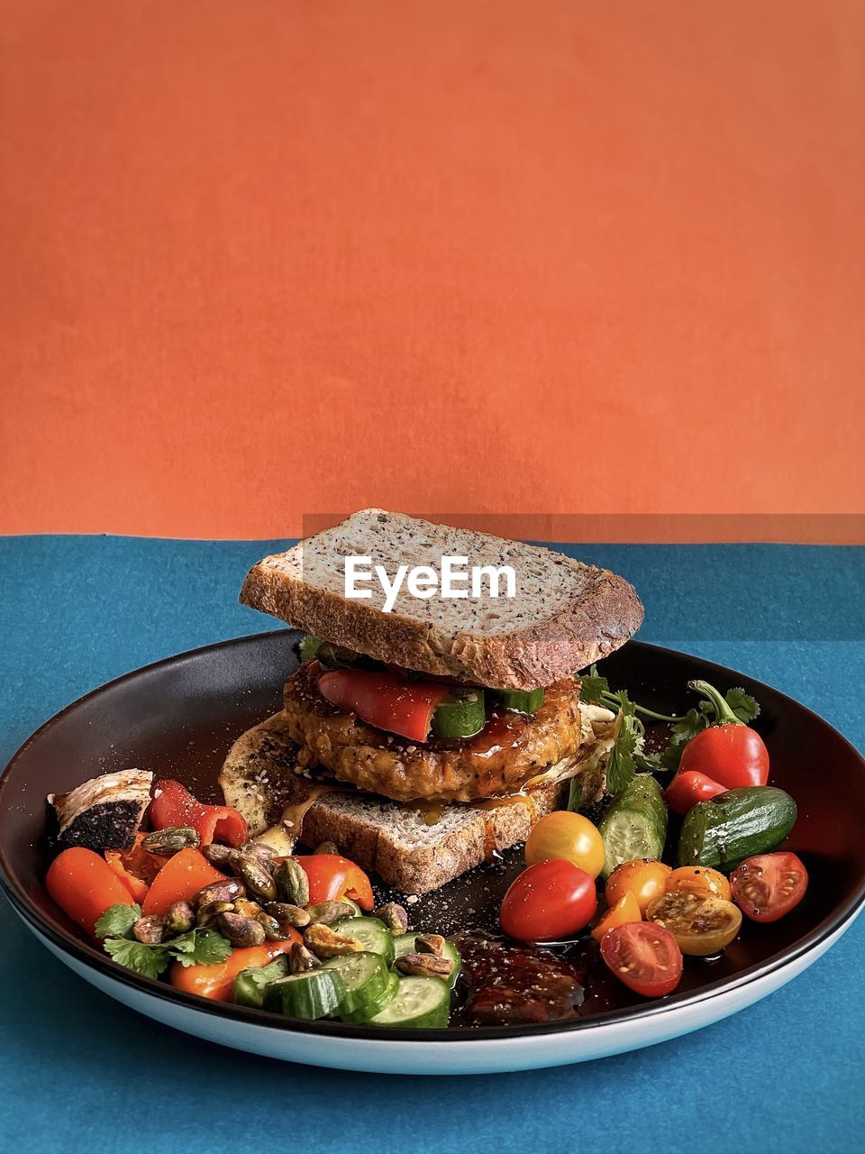 Close-up of veggie burger sandwich and fresh salad on black plate on colored background.