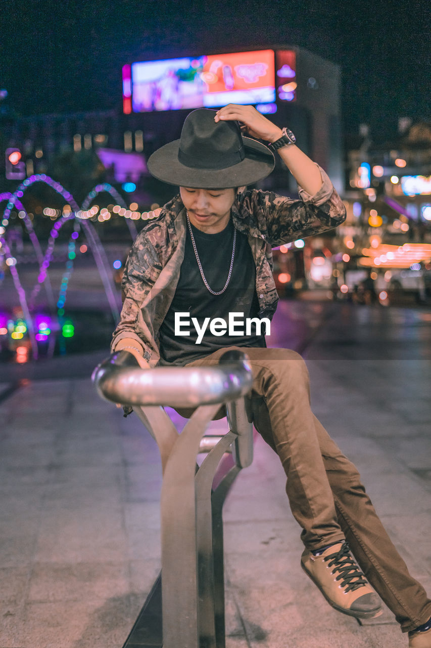 Young man sitting on railing in city at night