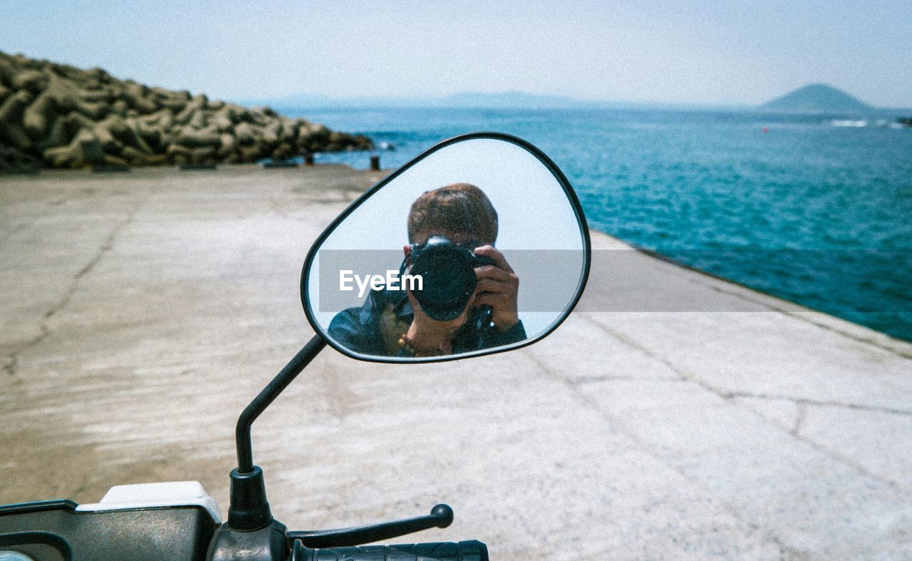Man photographing while reflecting on side-view mirror