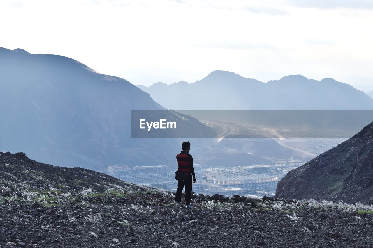 Rear view of man standing on mountain against sky