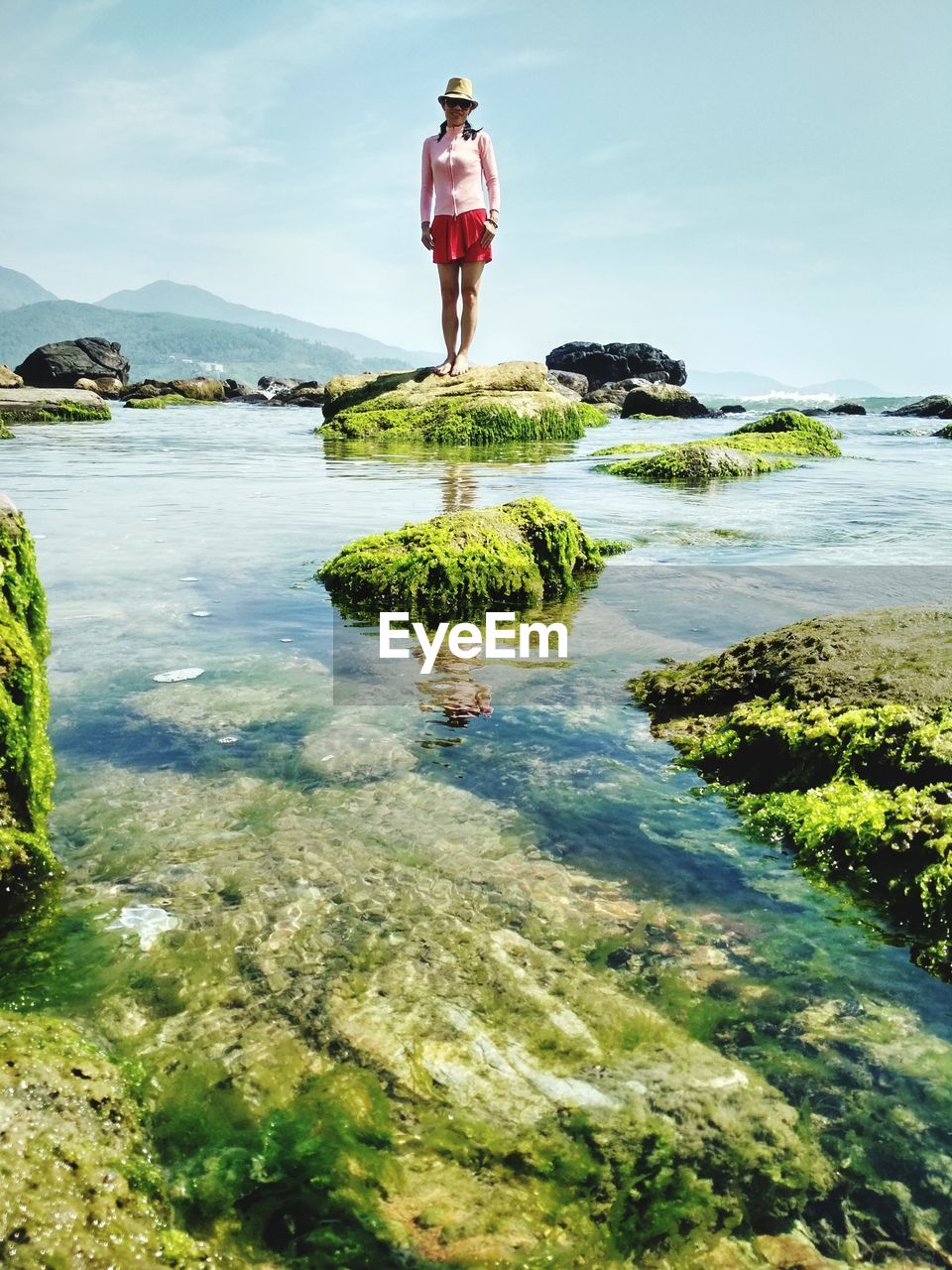 Woman standing on rock in lake against sky