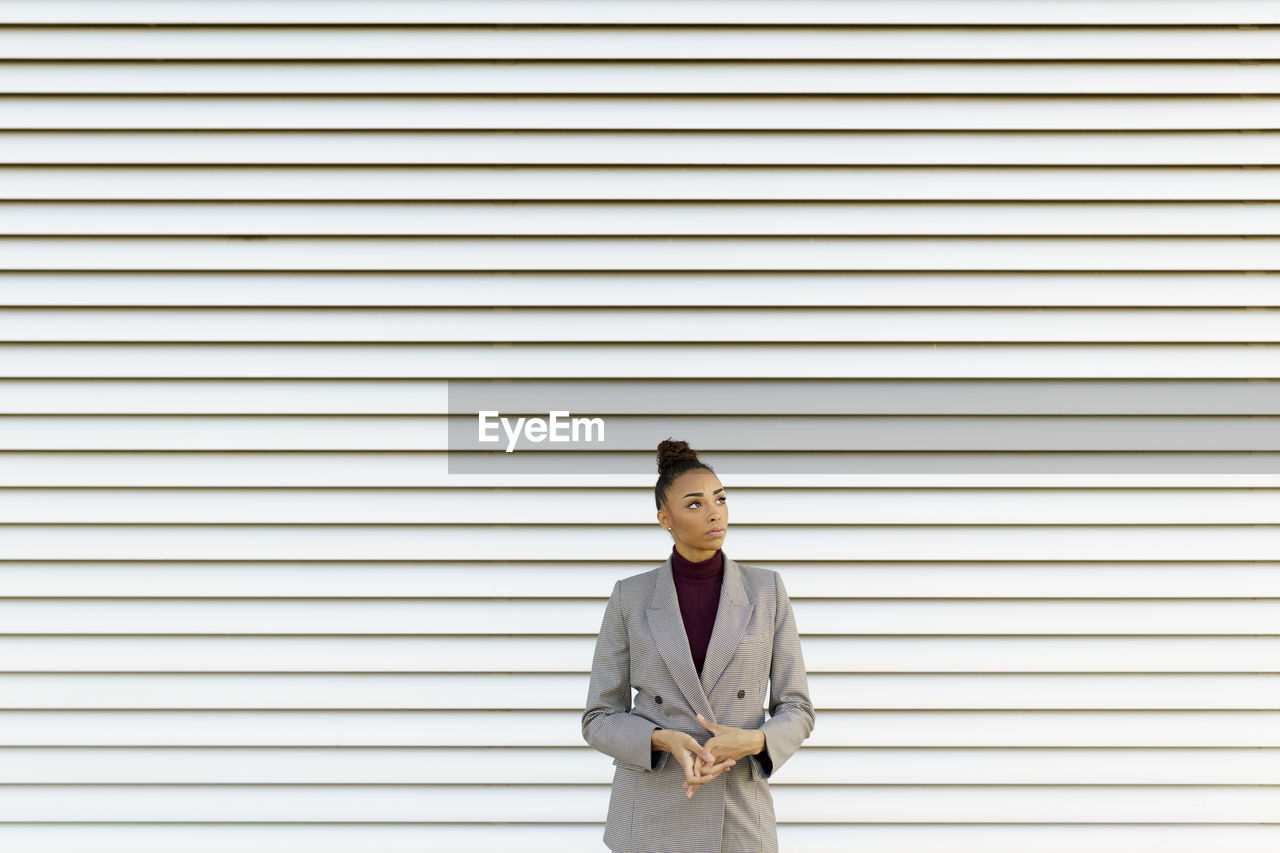 Thoughtful businesswoman looking away while standing against striped wall