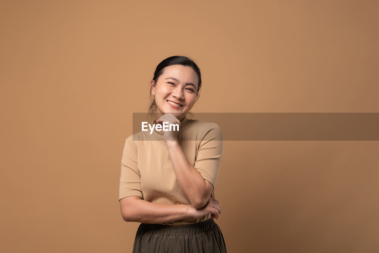 adult, studio shot, one person, women, colored background, indoors, smiling, portrait, emotion, copy space, business, happiness, businesswoman, standing, front view, waist up, female, arms crossed, young adult, looking at camera, photo shoot, cheerful, looking, hairstyle, positive emotion, person, three quarter length, brown hair