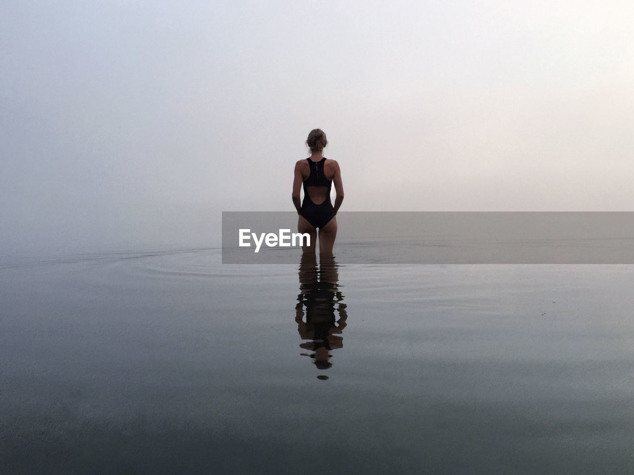 Rear view of woman in swimwear amidst sea during foggy weather