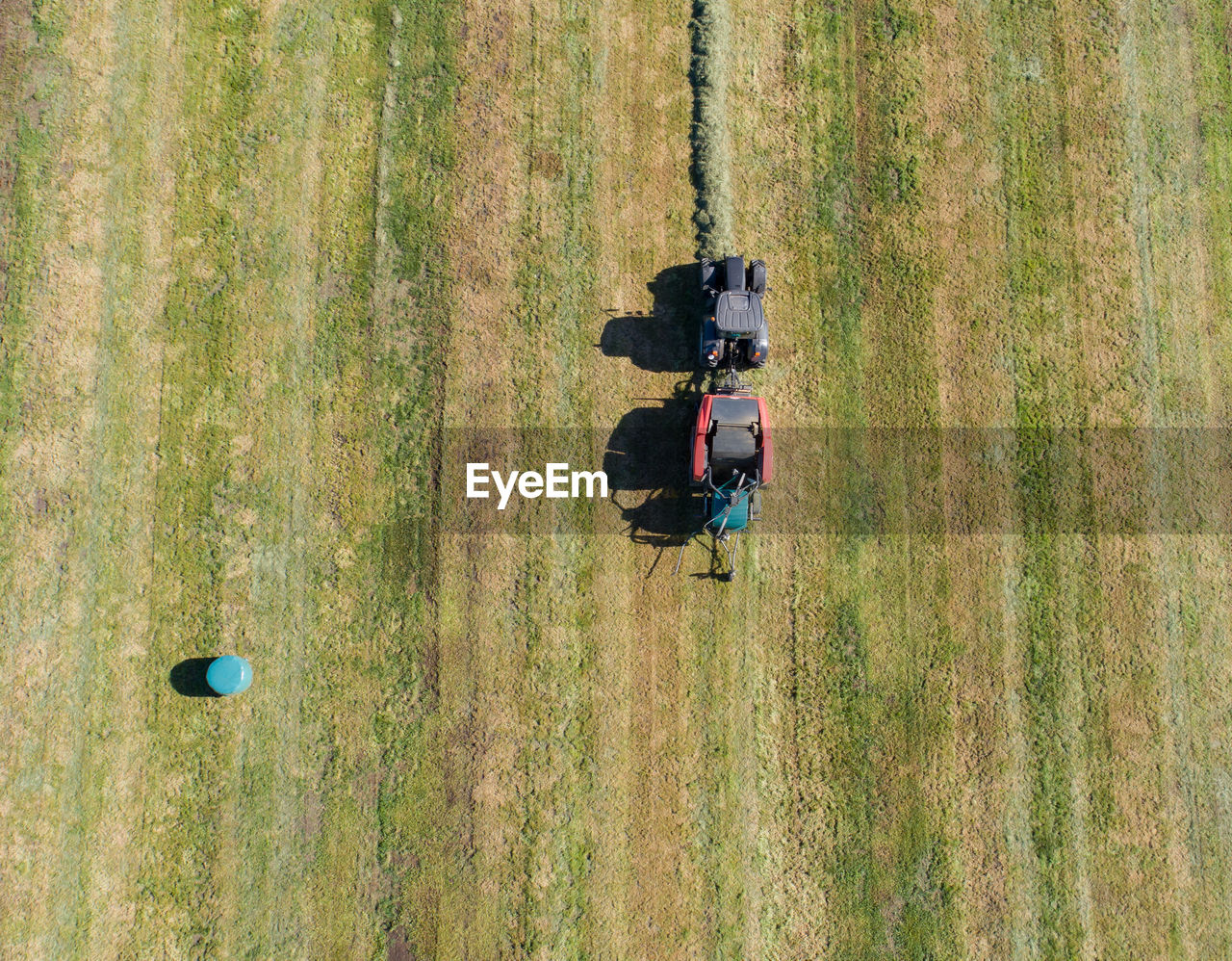 Black tractor with a red straw chamber press during the straw harvest on a mown field