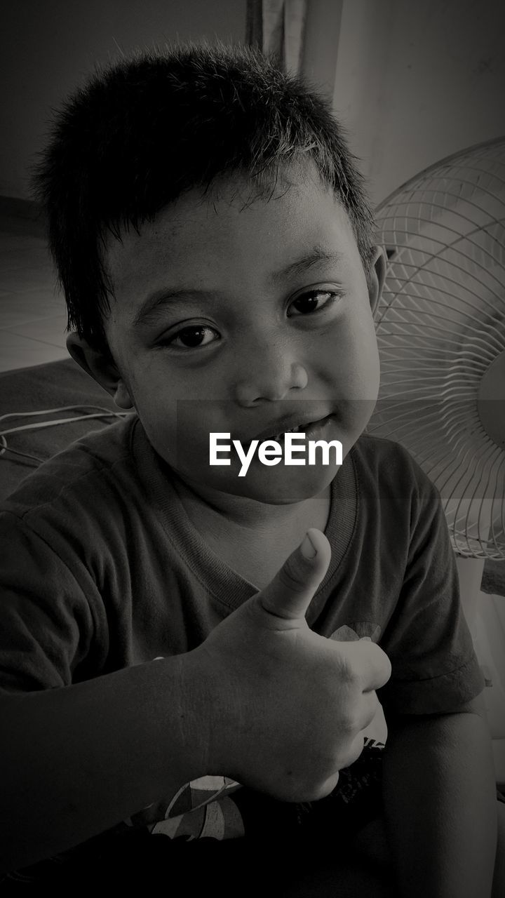 Portrait of cute boy showing thumbs up while sitting at home