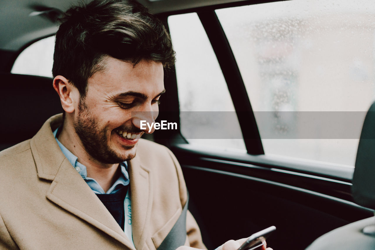 Close-up of happy businessman using phone while traveling in car