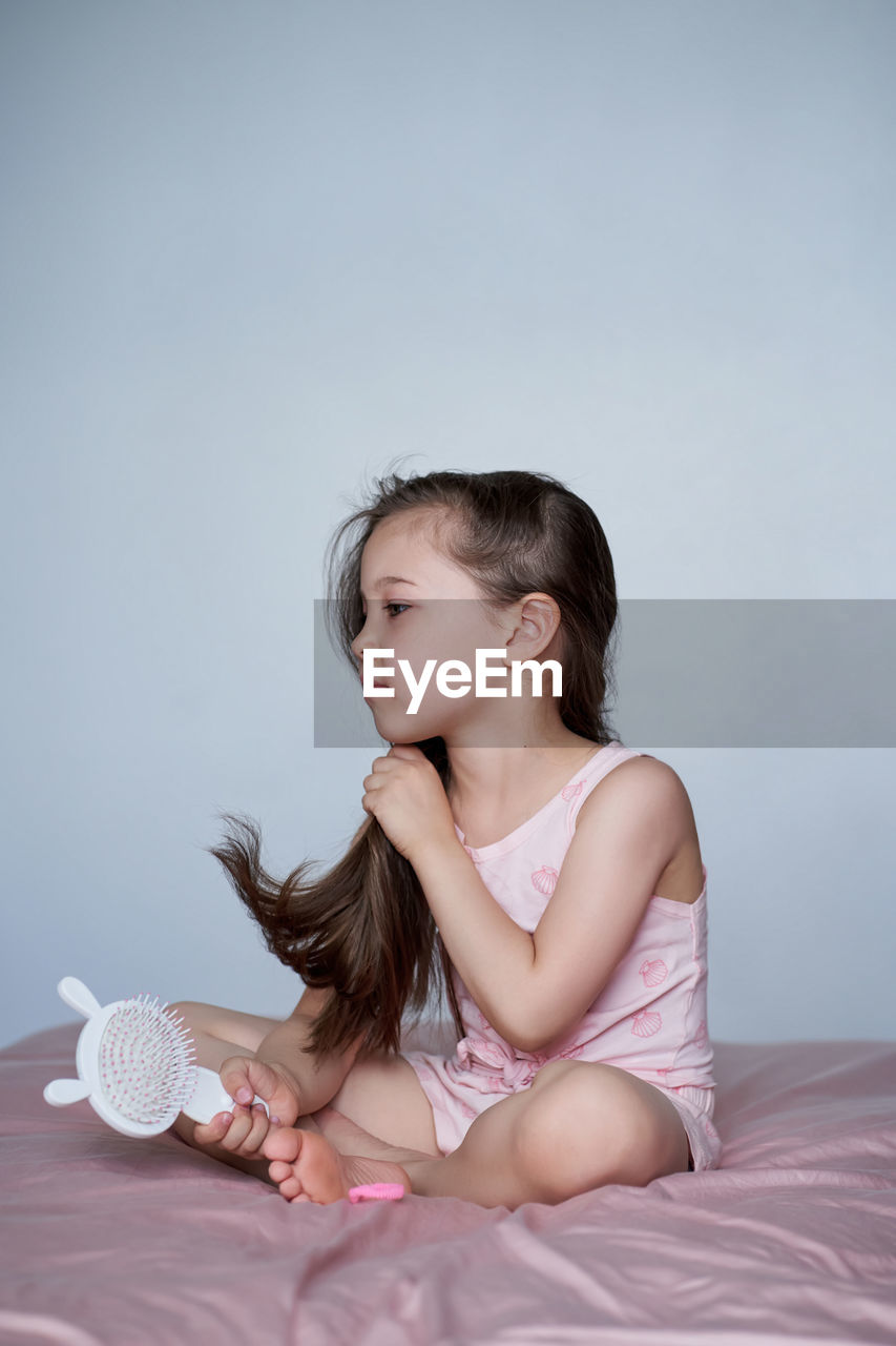 The girl is sitting on the bed and combing her long hair.