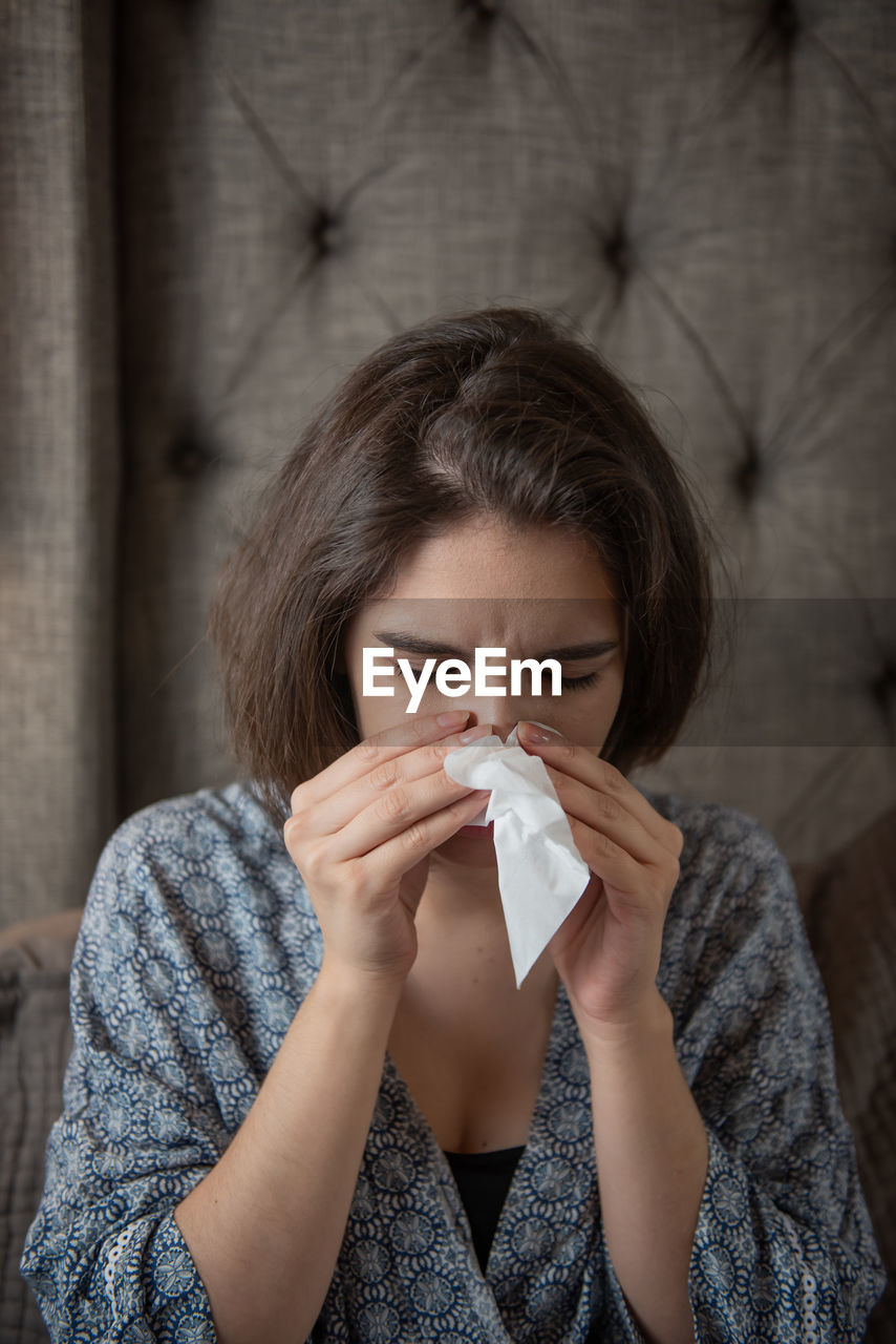 Woman with tissue paper sneezing at home