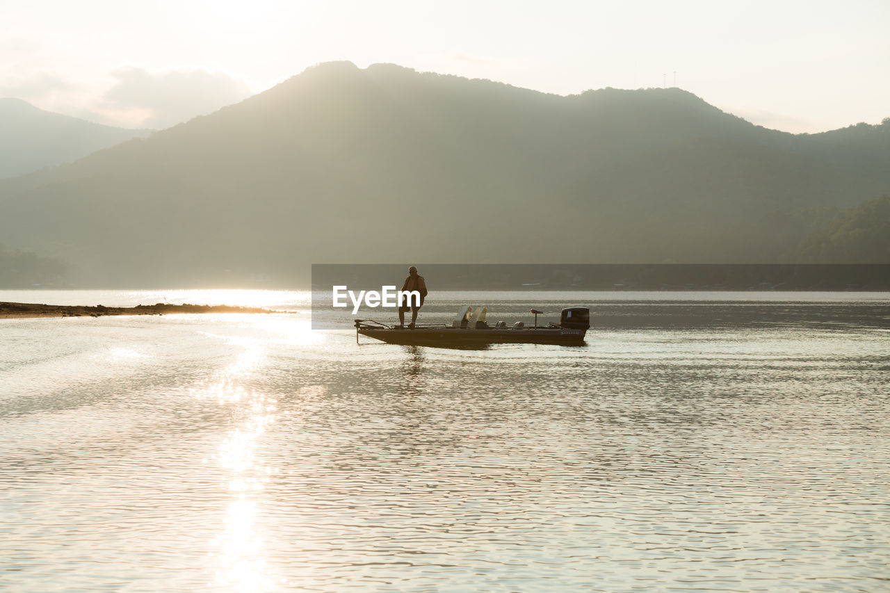 SILHOUETTE BOAT IN CALM SEA AGAINST MOUNTAINS