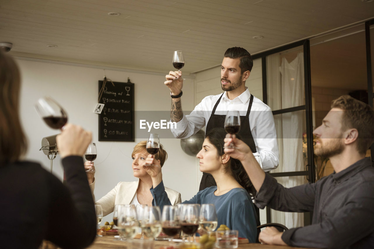 Man standing by people and analyzing wineglass at table