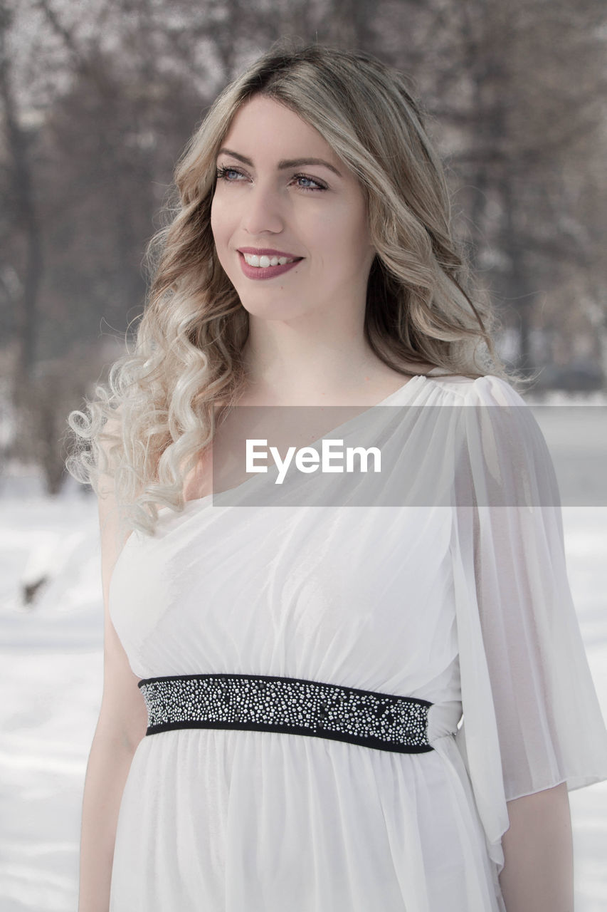 Smiling young woman looking away while standing on snow covered field