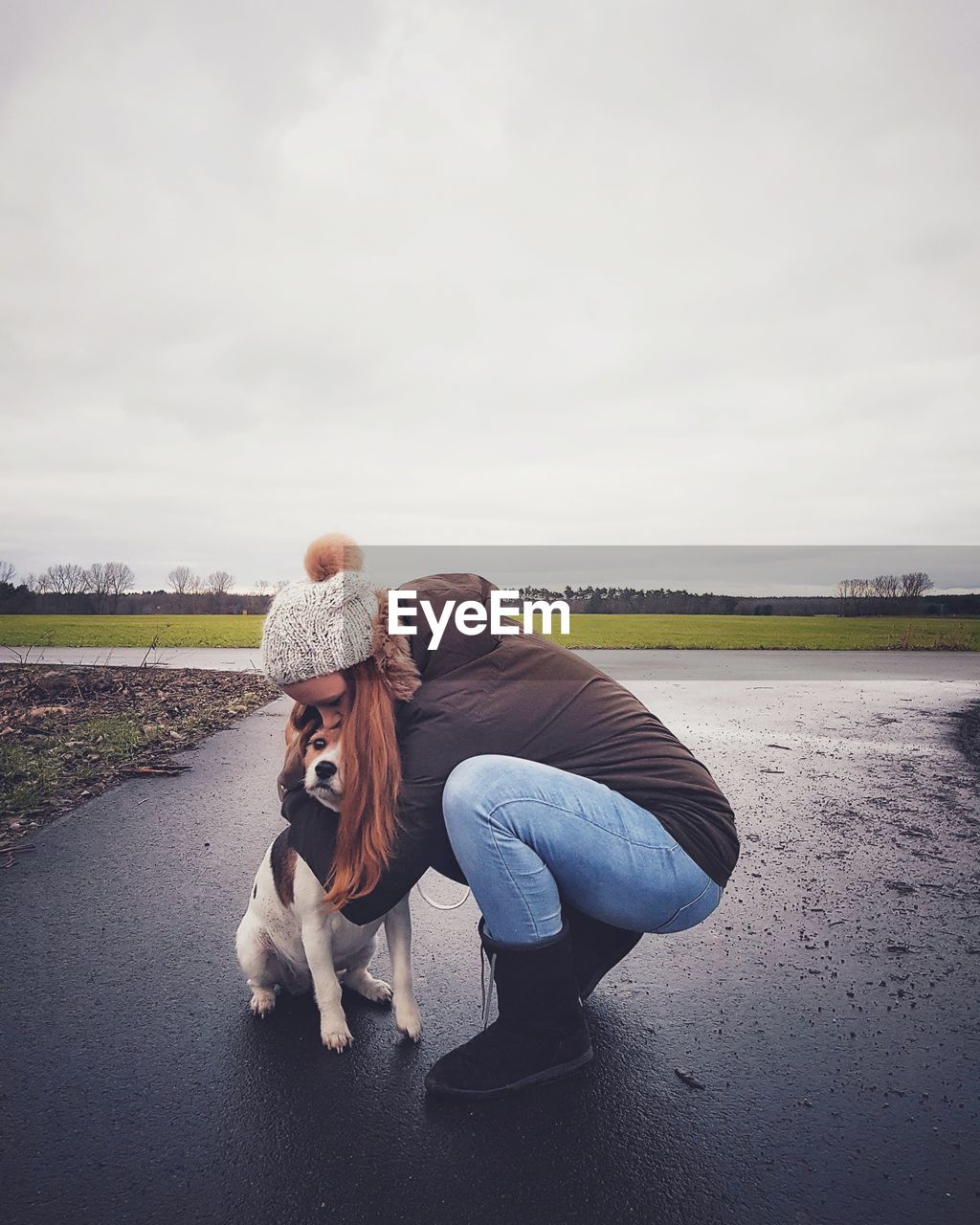 Woman with dog crouching on street against sky