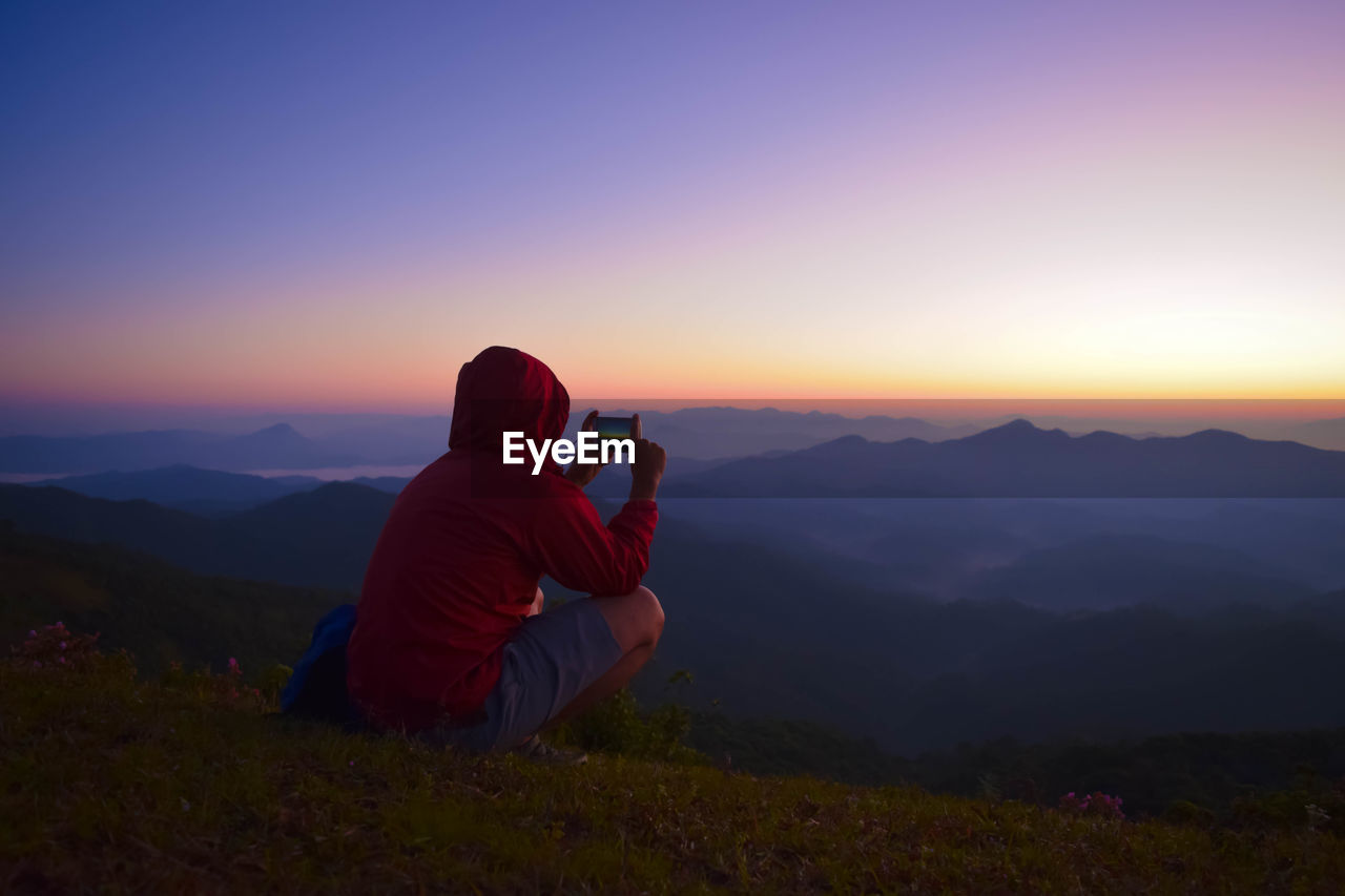 Rear view of man photographing on mountain during sunset