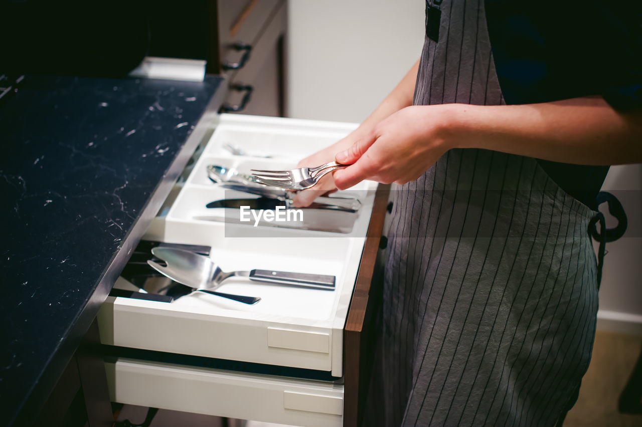 Midsection of woman holding eating utensils at kitchen