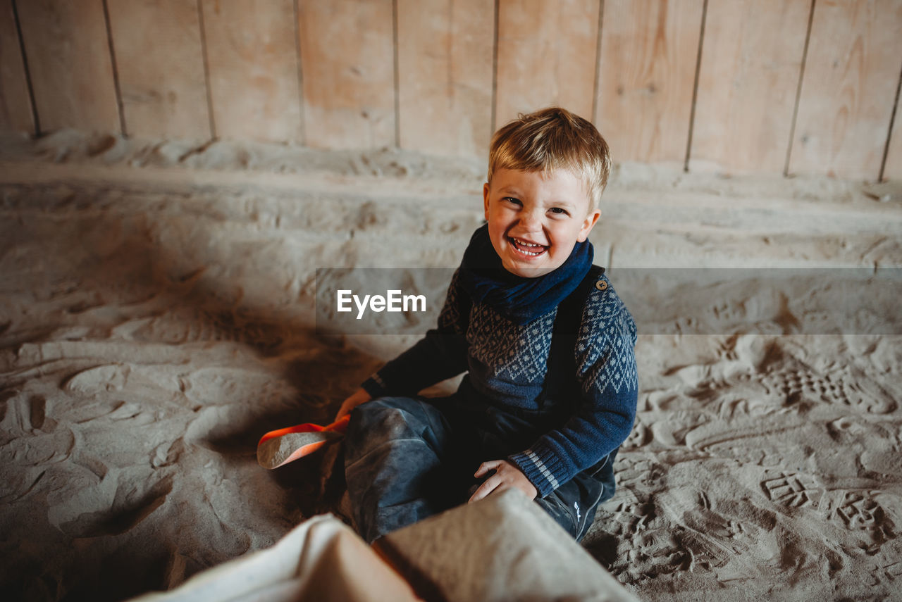 Little boy smiling playing in sand in winter with shovel in hand