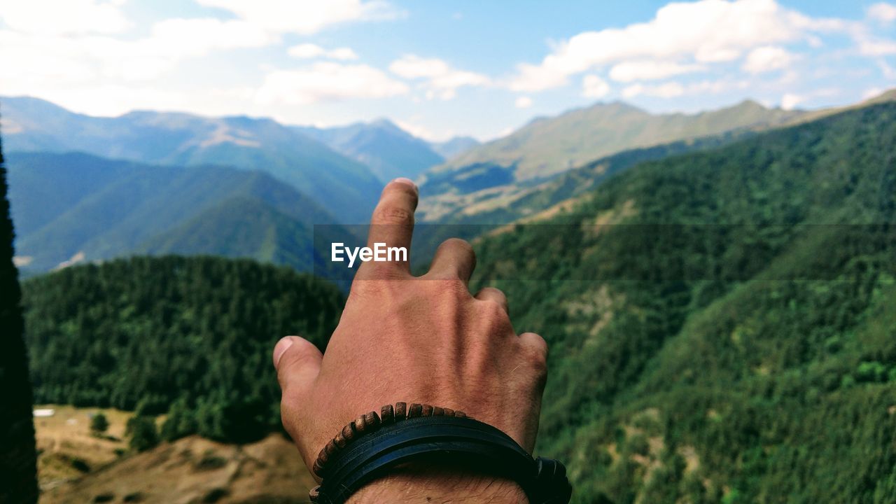 Cropped hand of man against mountain range