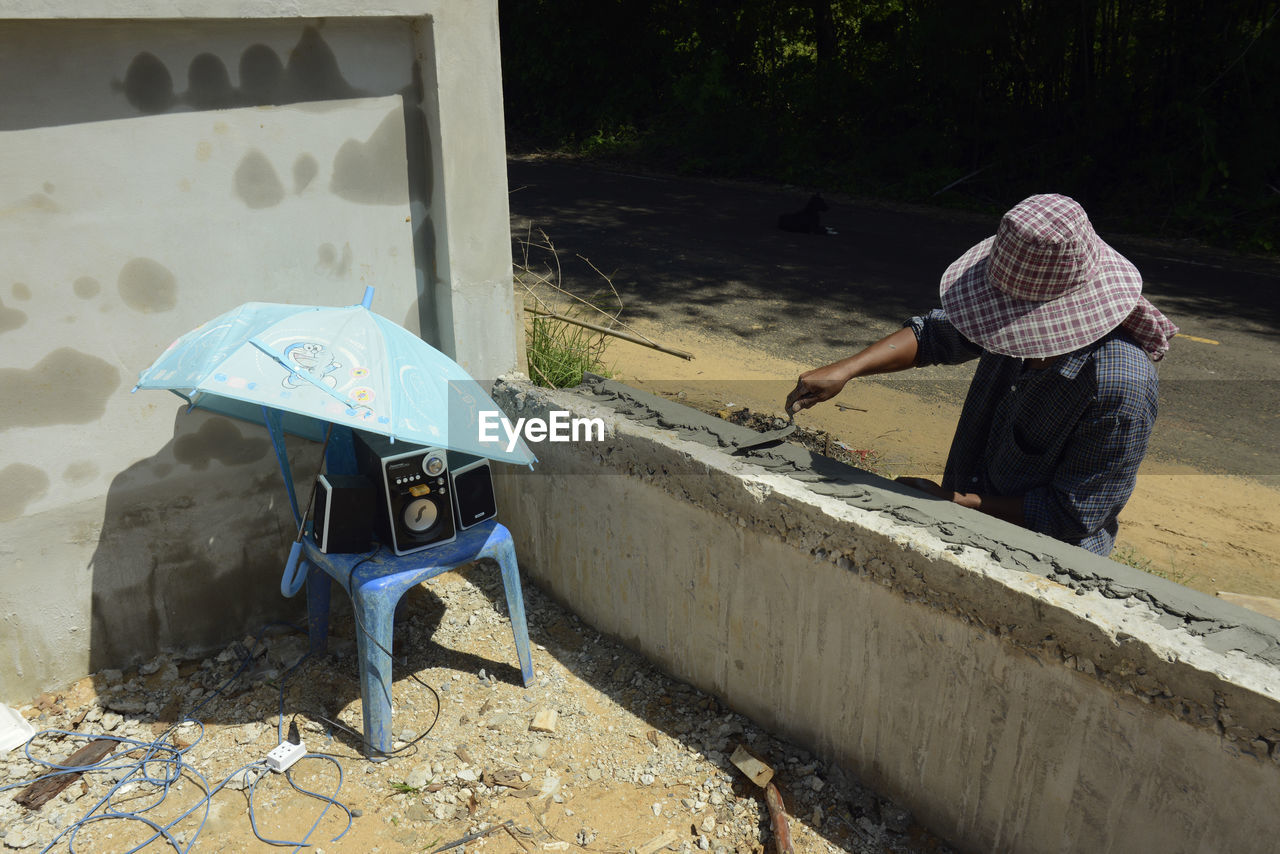 High angle view of worker adding cement on wall by umbrella protecting speakers