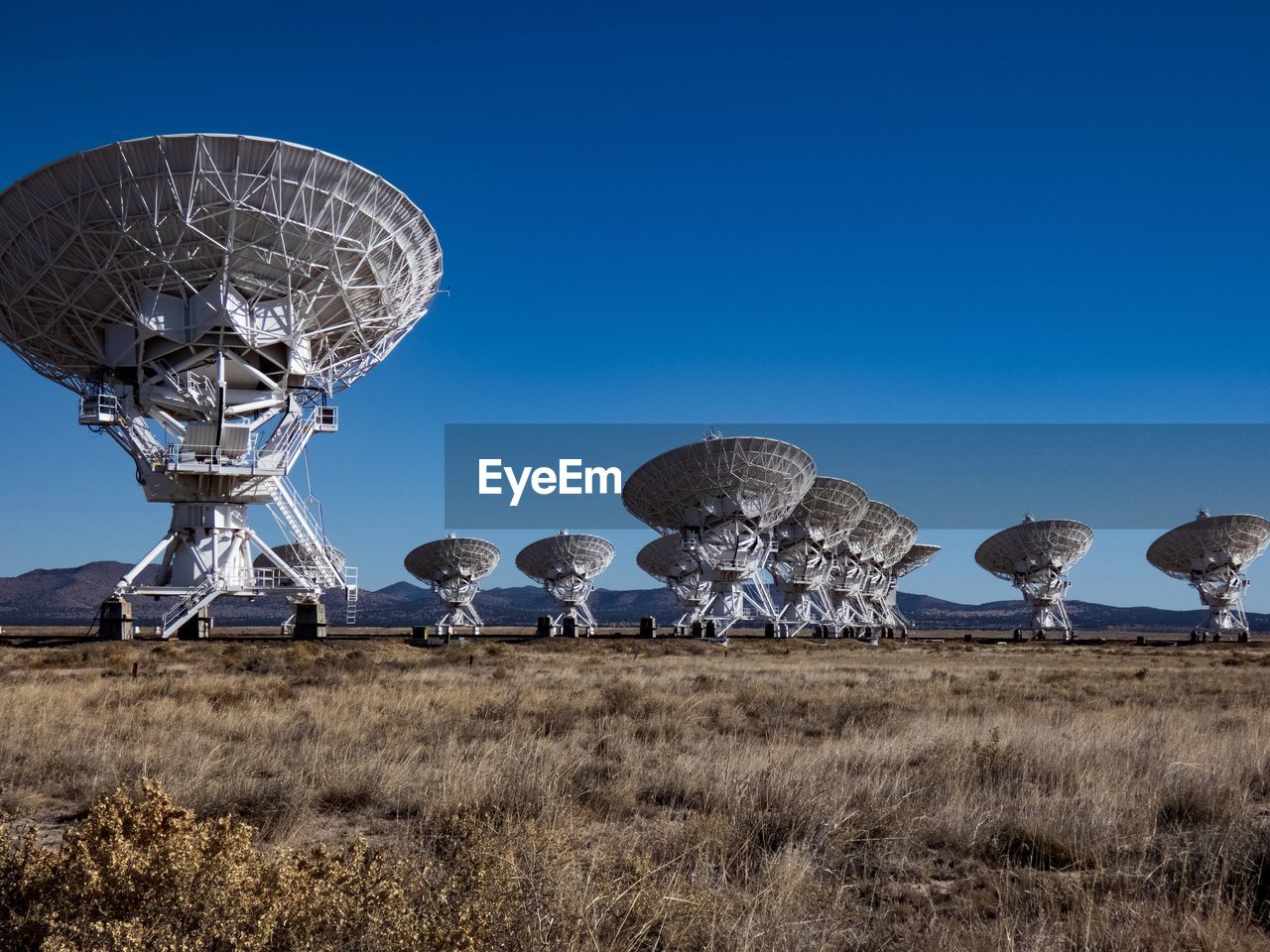 Low angle view of satellite dishes on field against clear blue sky