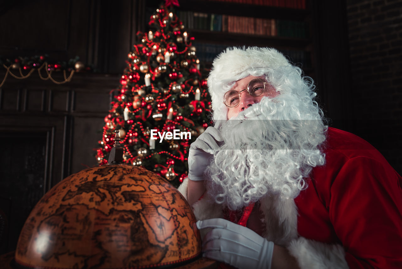 Man wearing santa claus costume by globe at home