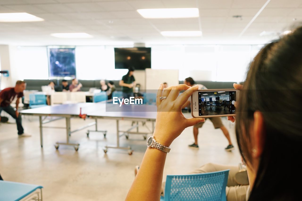 MIDSECTION OF WOMAN PHOTOGRAPHING WITH MOBILE PHONE IN OFFICE