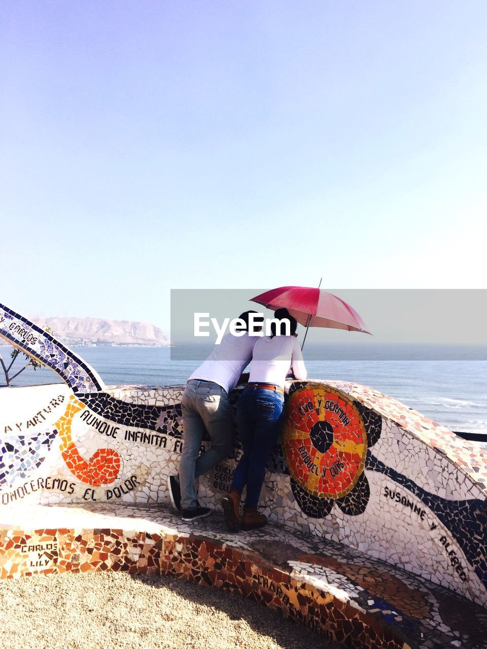 Rear view of couple standing by retaining wall against sea