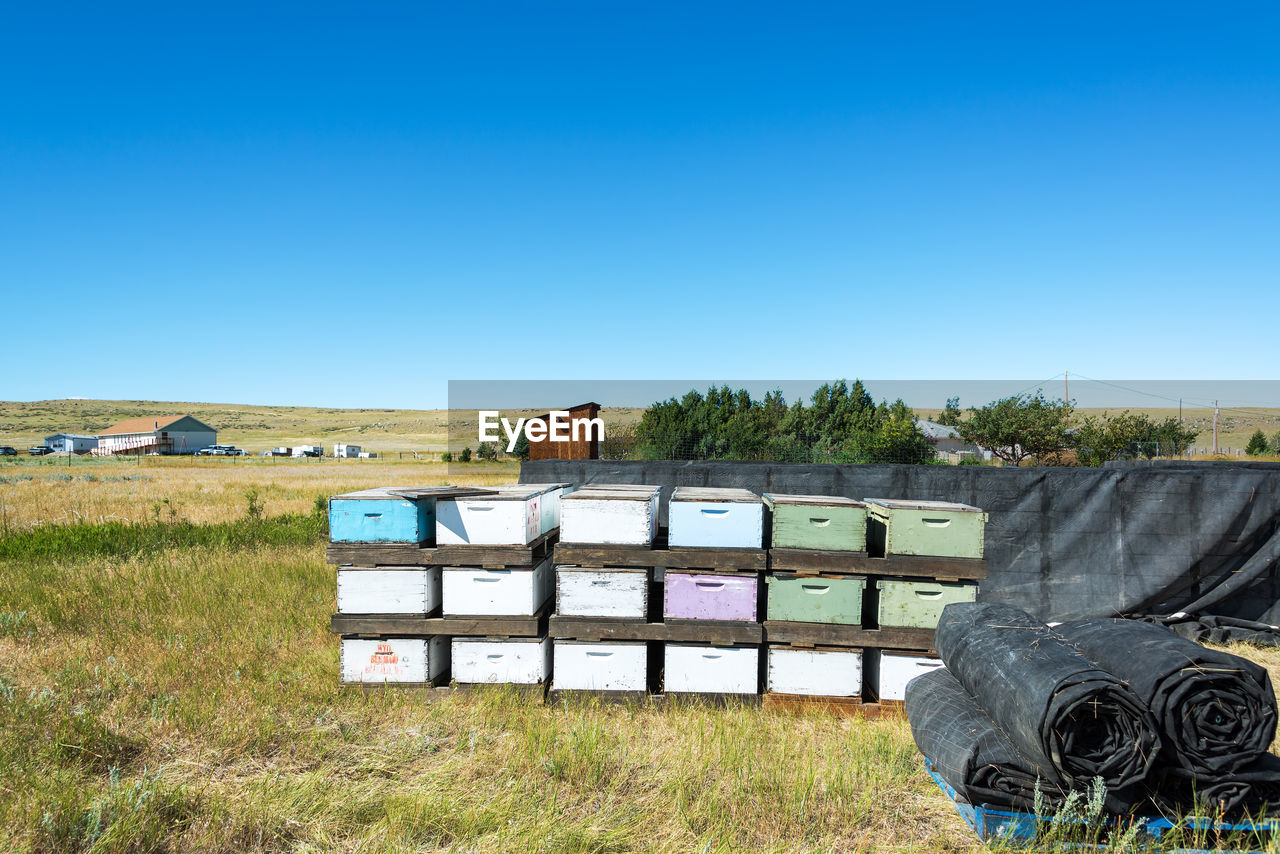 Beehives on grassy field against clear blue sky