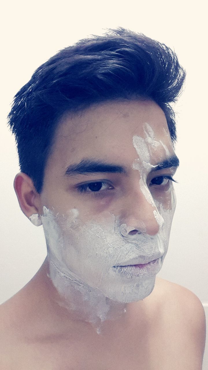 Close-up of young man with messy paint on his face against white background