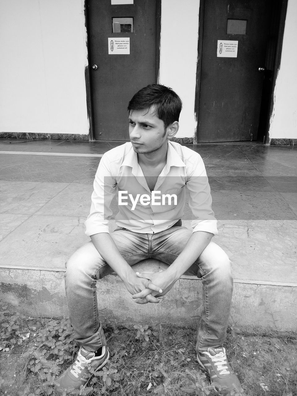 Full length of thoughtful young man sitting against closed doors