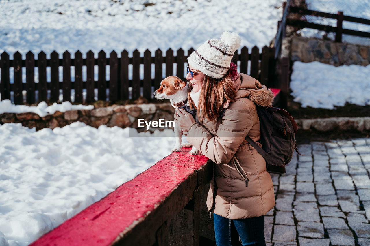 Woman holding dog on retaining wall during winter