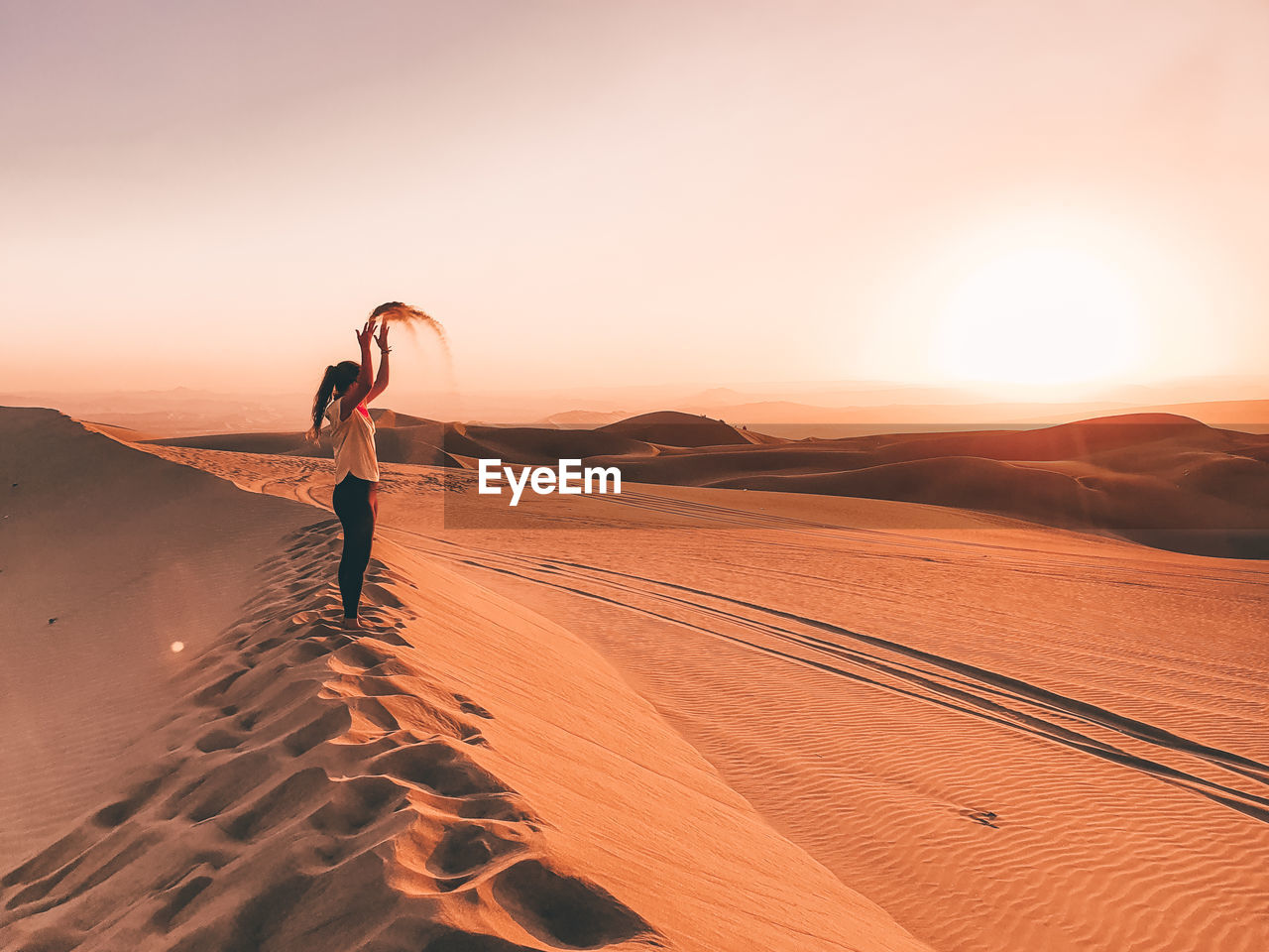WOMAN STANDING ON SAND DUNE IN DESERT AGAINST SKY