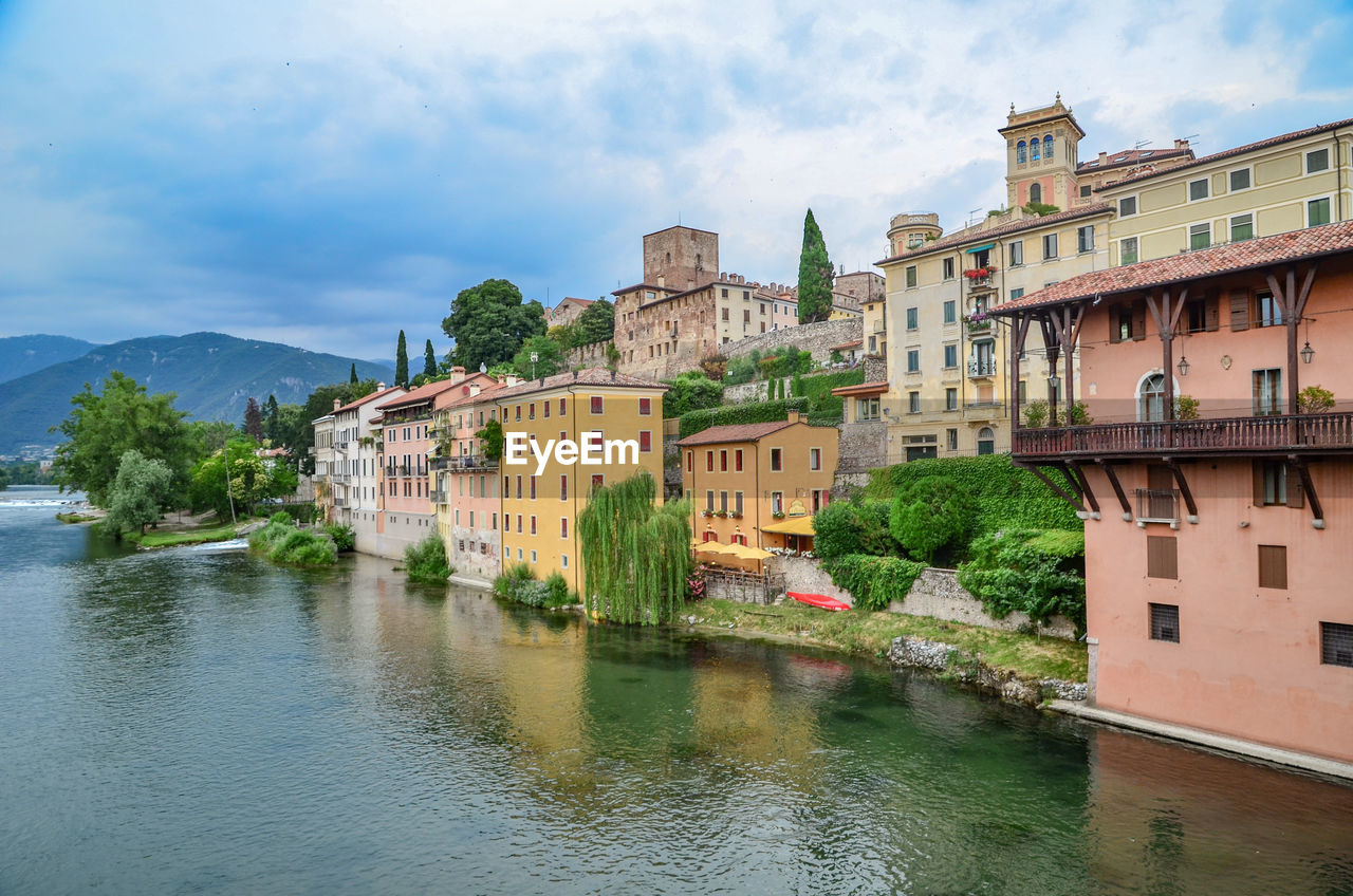 Buildings by river against sky in town