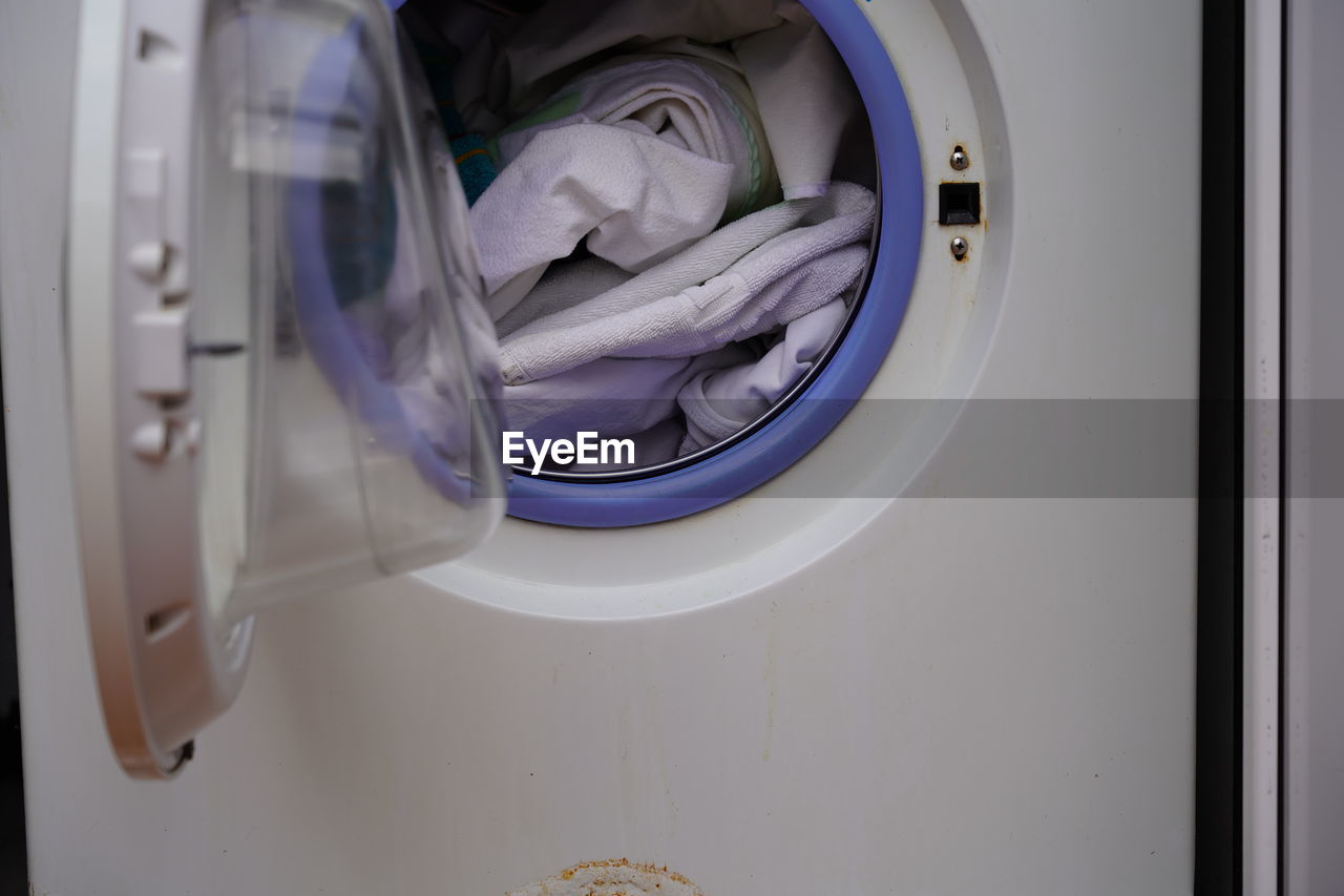 Close-up of open door of washing machine filled with dirty bed sheets