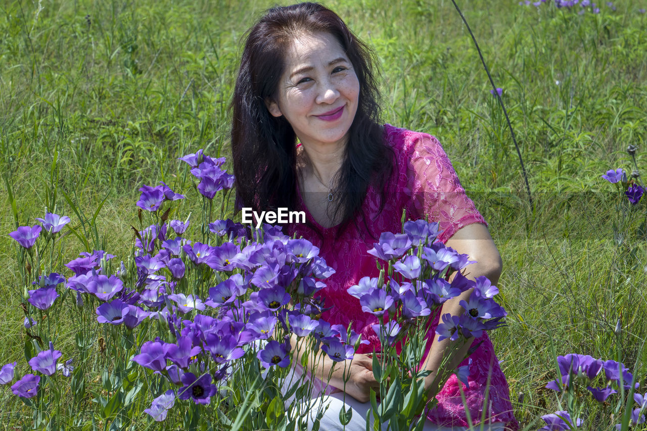 PORTRAIT OF A SMILING YOUNG WOMAN IN PURPLE FLOWERING PLANTS