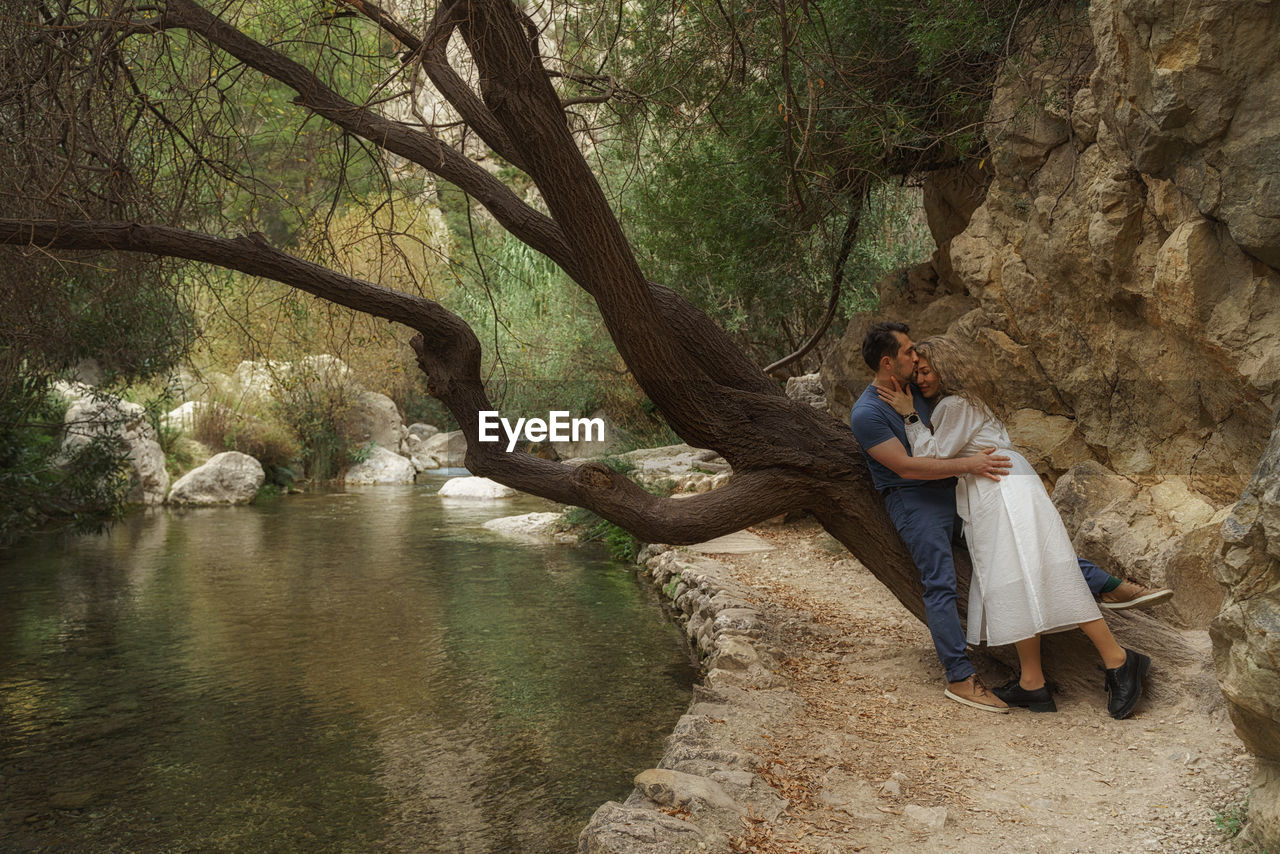 Full length of young woman and man standing against tree