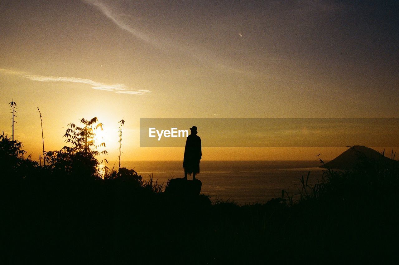 Silhouette person standing at beach against sky during sunset