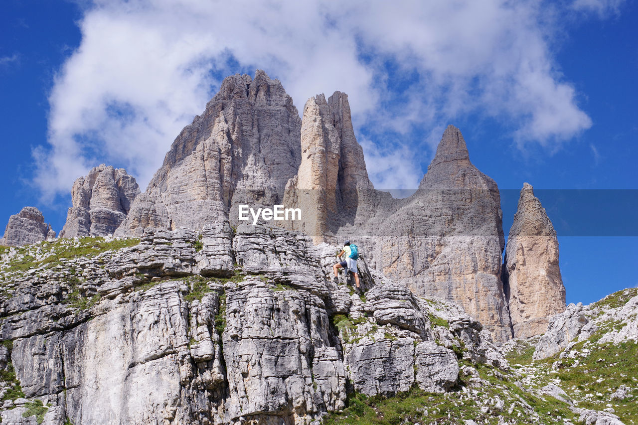 Low angle view of person on rocky mountain against sky