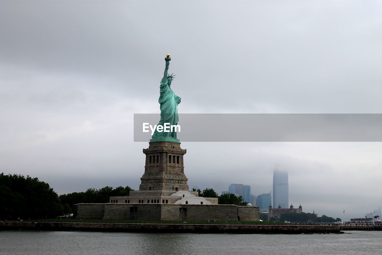 STATUE OF LIBERTY IN CITY AGAINST SKY