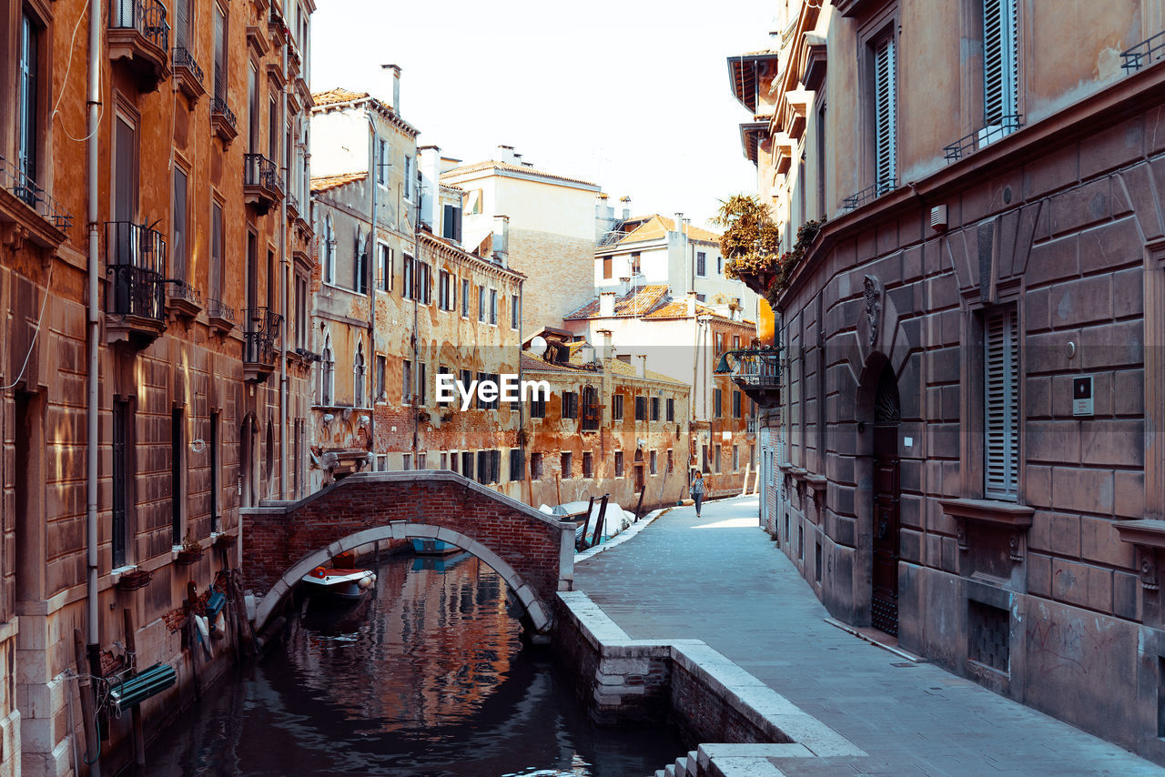 Arch bridge over channel amidst buildings against clear sky