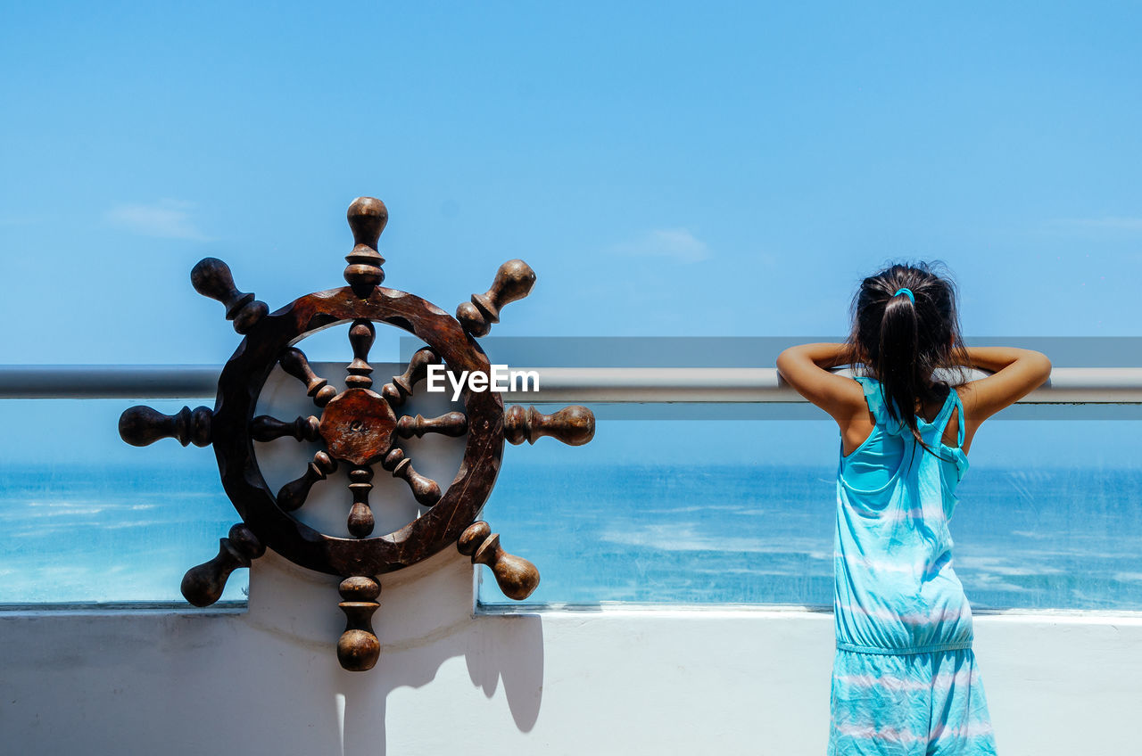 Rear view of girl standing by railing against sea