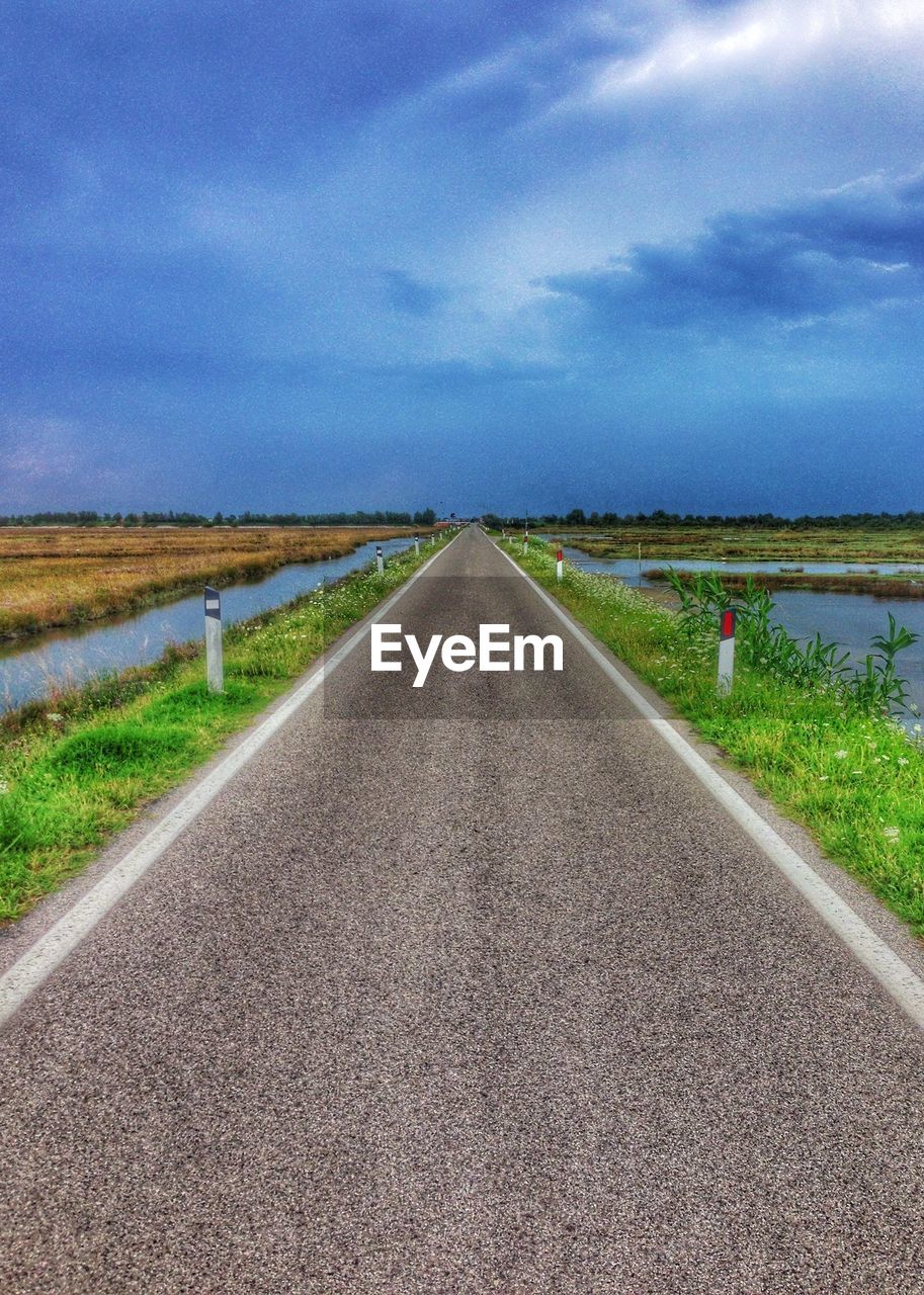 Road amidst field against blue sky