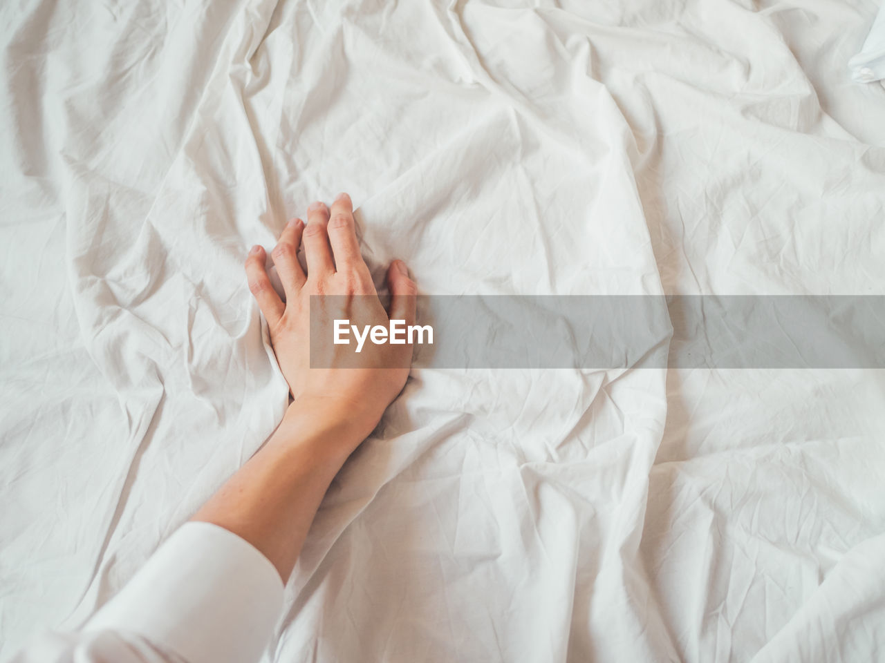 Woman's hand on background of crumpled bed sheet. creased white linen. woman touches unmade bed. 