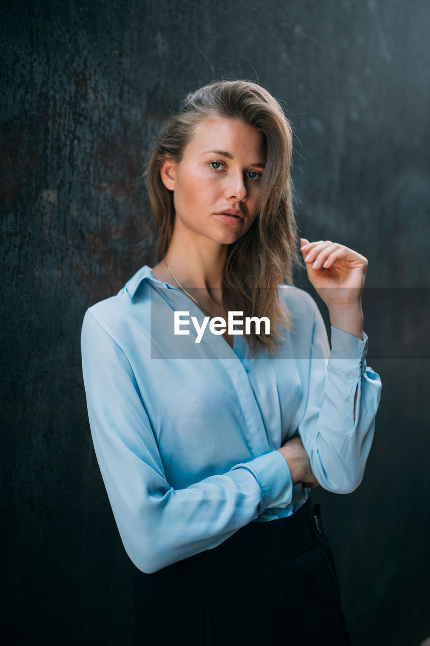 PORTRAIT OF A YOUNG WOMAN STANDING AGAINST WALL