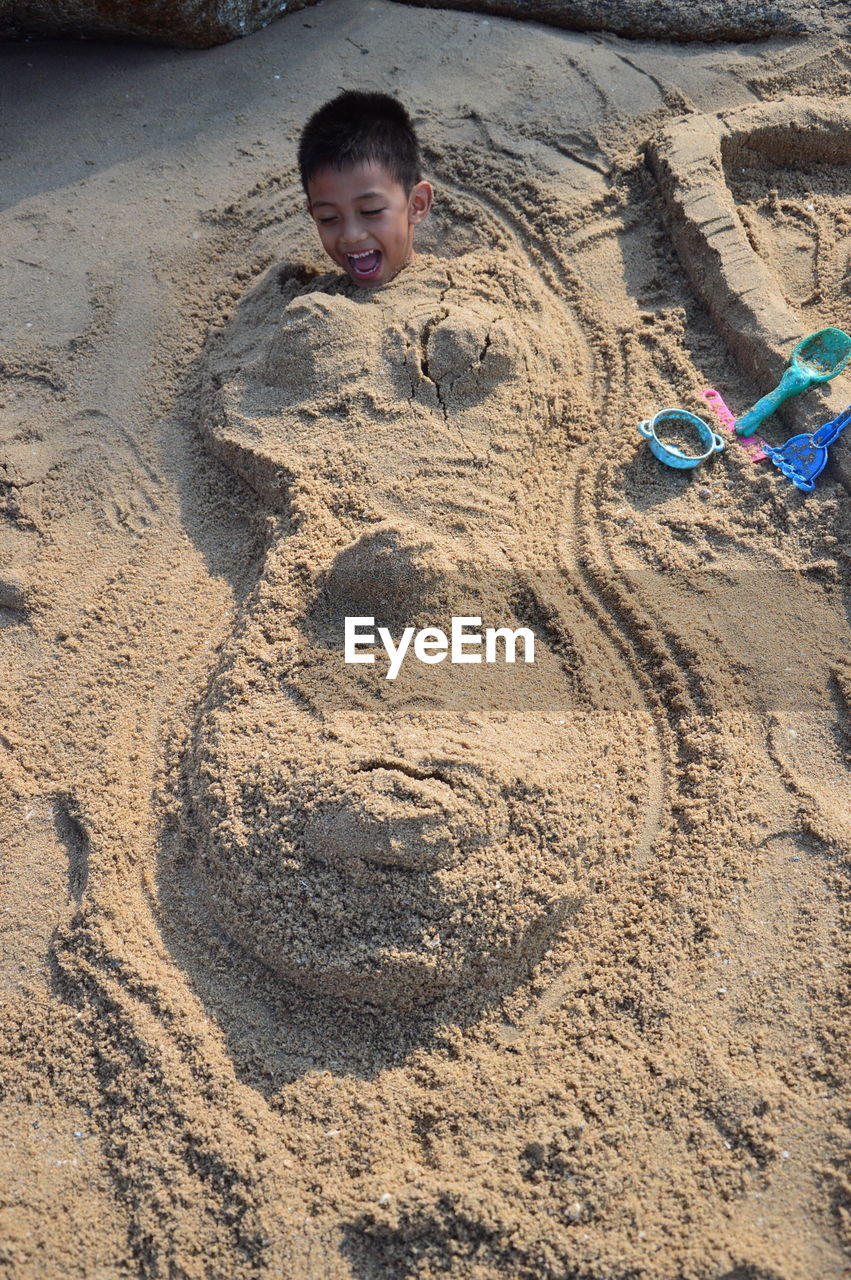 High angle view of playful boy buried in sand
