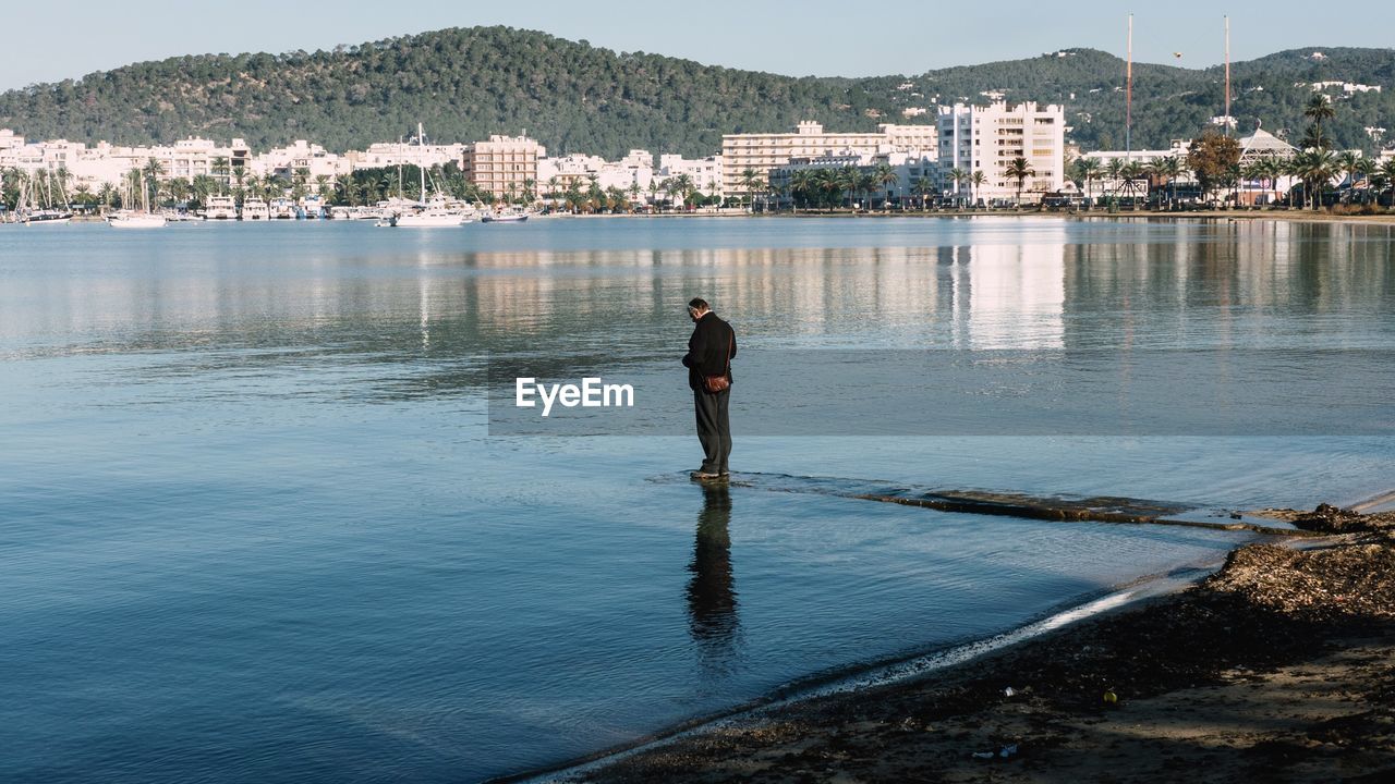 Man standing on pier amidst lake in city
