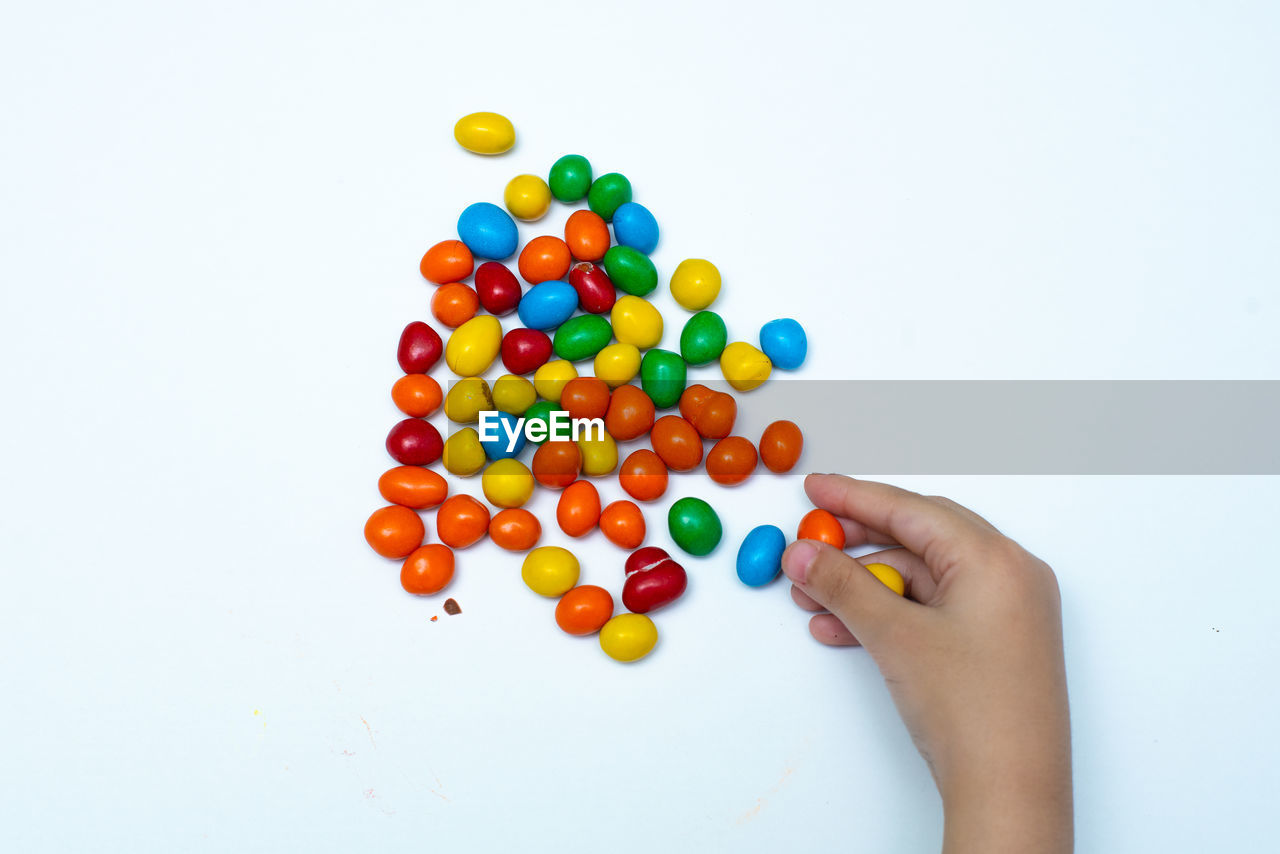 Cropped hand of person holding multi colored candies against white background