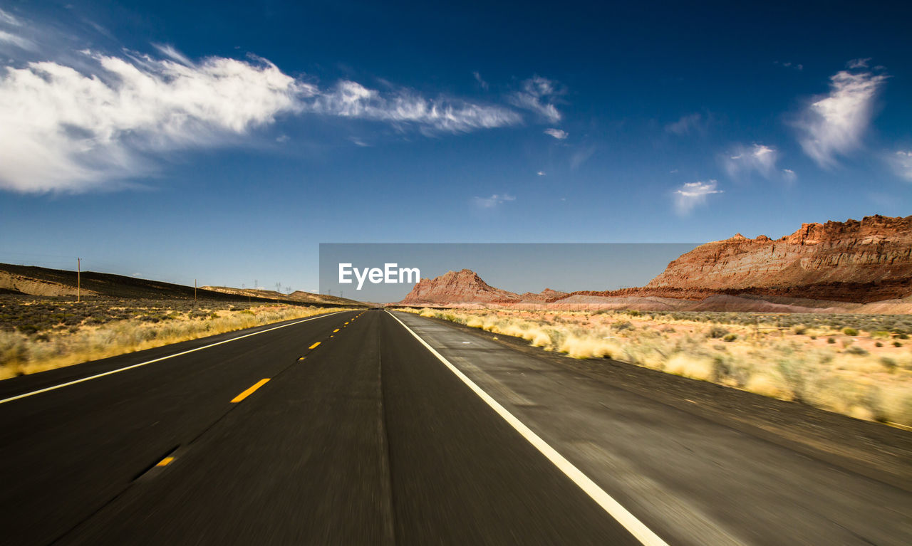 Country road on desert landscape against sky