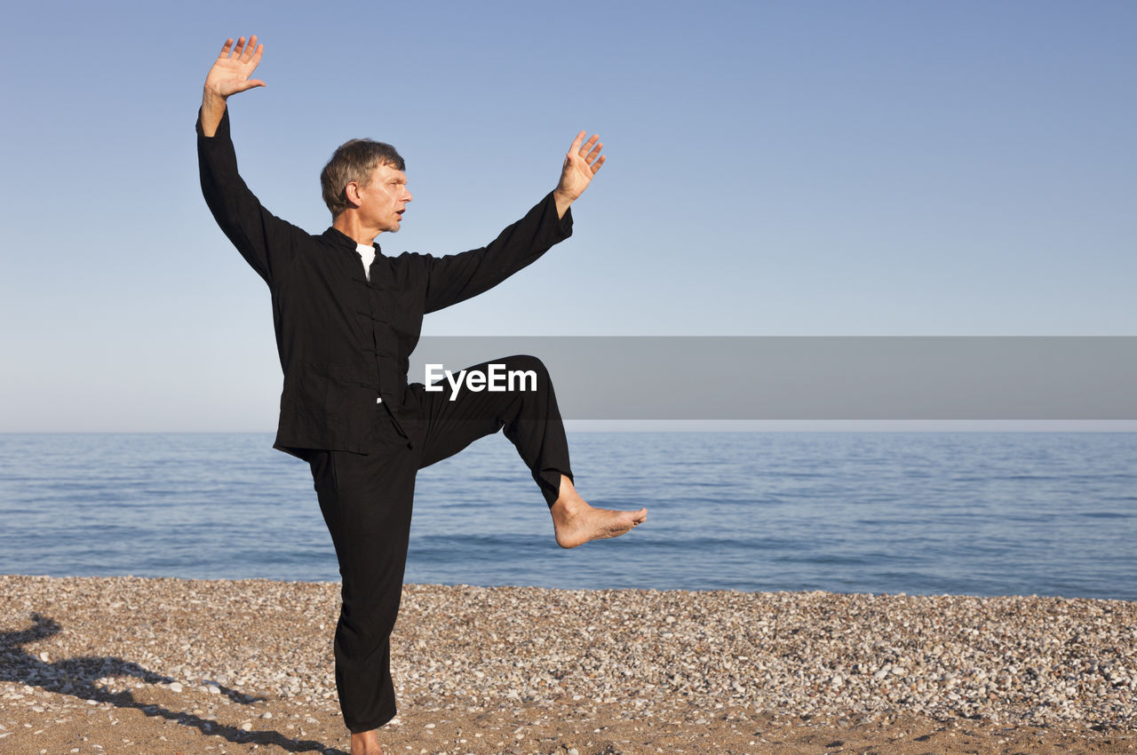 Full length of man doing martial arts on shore at beach